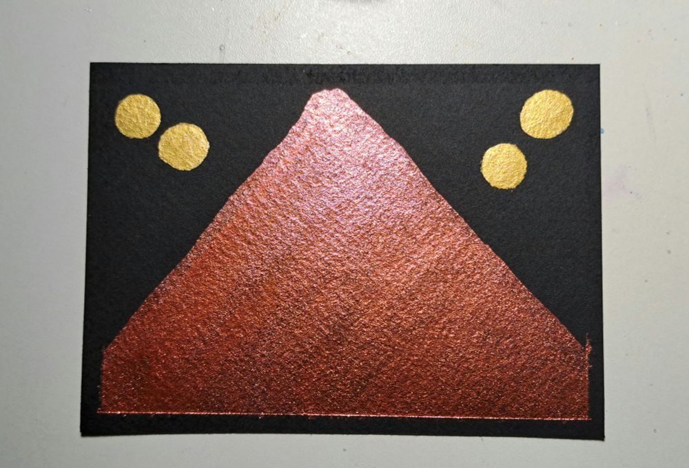 A rectangle of black watercolor paper with a steep metallic Red Mountain and two round gold moons to either side