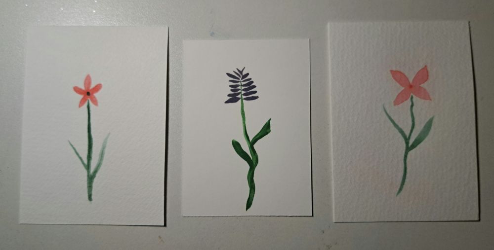 A photo of three small watercolor flowers, two orangey pink and one lavender