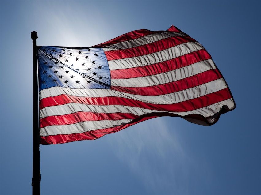 The Star Spangled Banner flag of USA flying in the wind with the sun behind it on a mostly blue sky