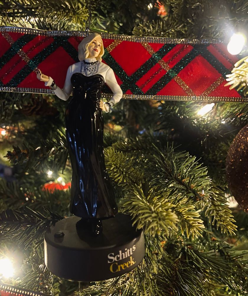 Photo of a lit Christmas tree adorned with ribbon and a Catherine O’Hara Schitt’s Creek ornament