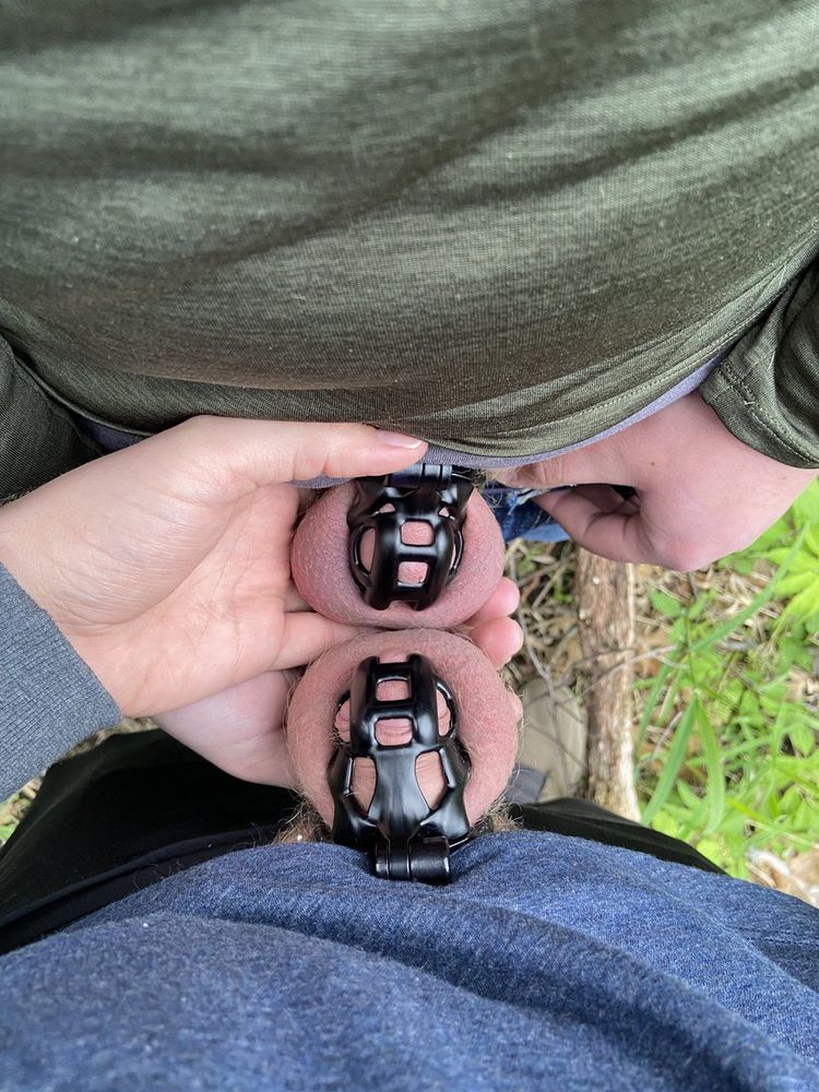 two men in black chastity cages standing with their cages touching
