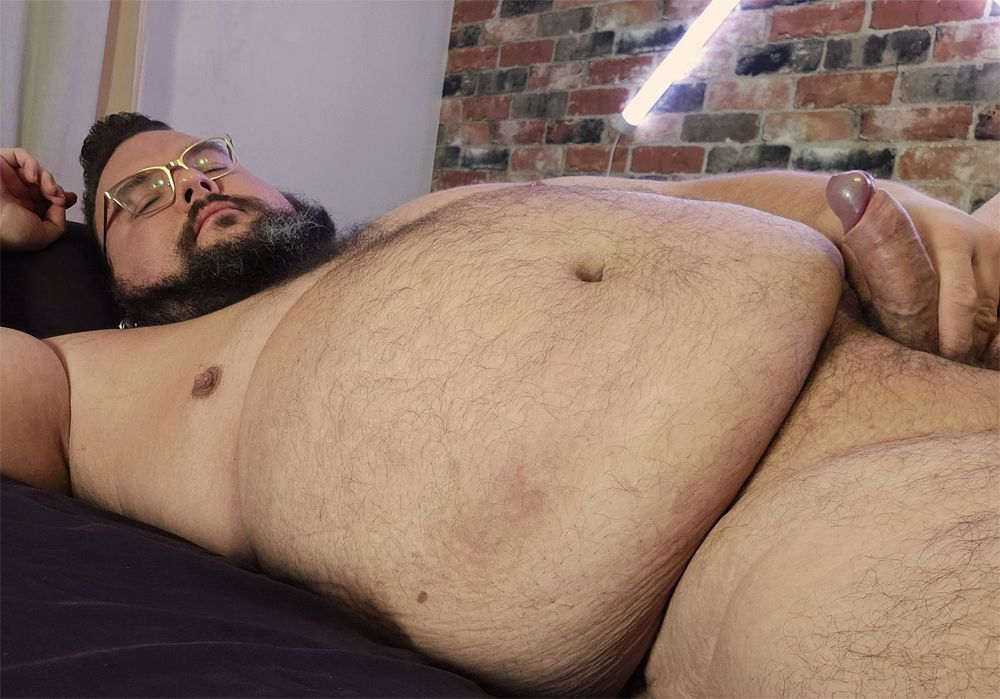 A large person laying down on a bed, lost in thought while holding their erection.