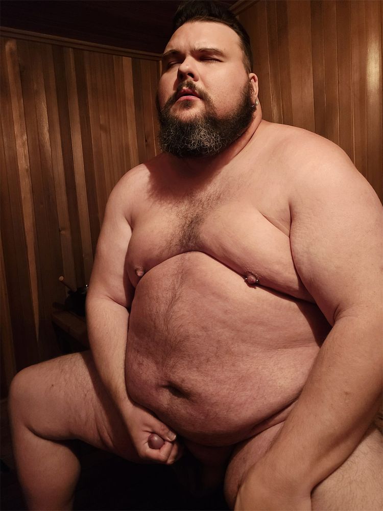 A large person sitting in a sauna, masturbating and lost in pleasure.