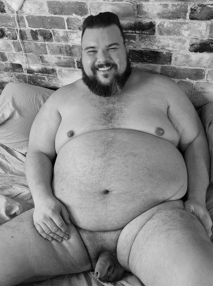 A naked large person with a full view of their body while propped up against a wall.