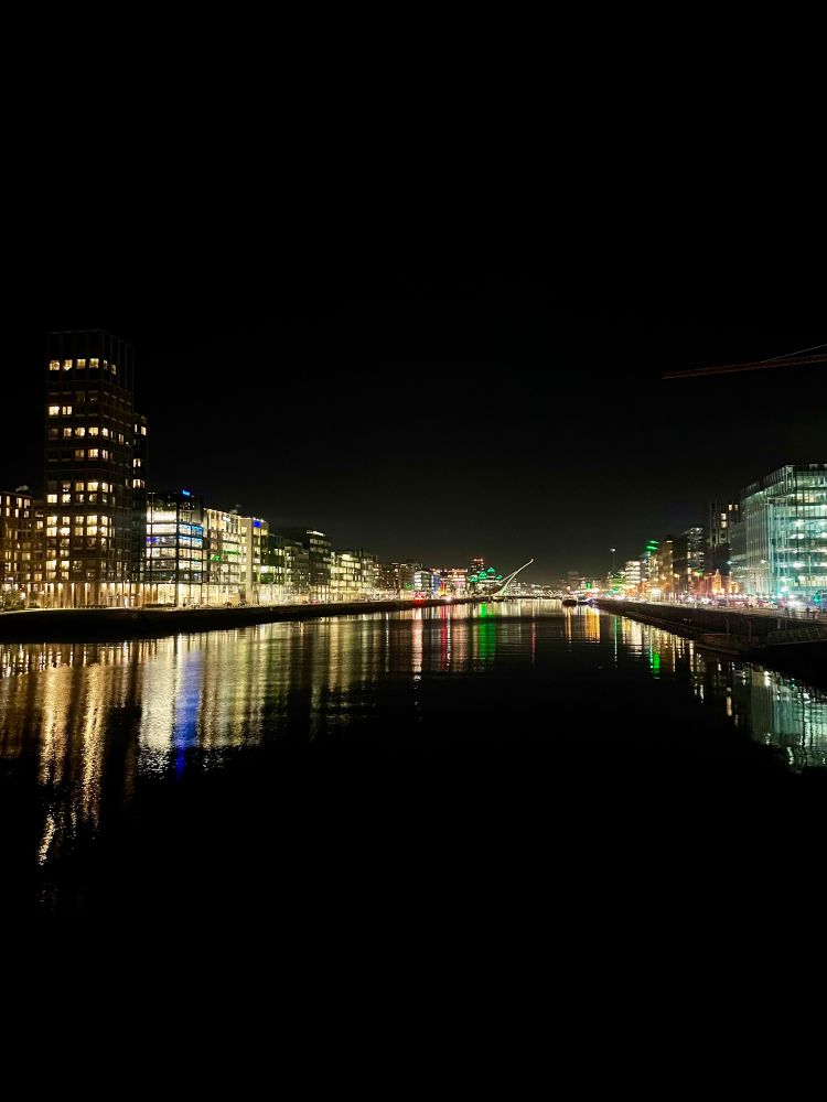 Same view at night. The lights of the buildings reflect into the water, against a black night sky. 