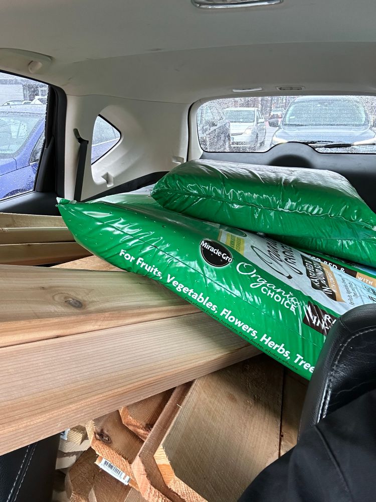 The back of a small SUV filled with cedar 2x4s and fence pickets as well as 300 quarts of soil. 