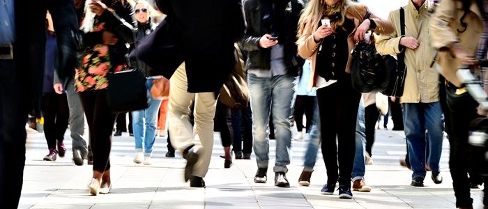 People walking down a busy street. Some are looking at their mobile phones.