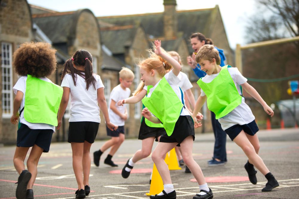 Children running around in a school playground. Some children are wearing hi-vis vests.