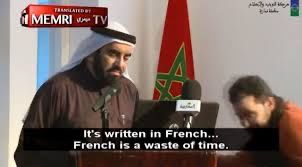 Man at a microphone with the Moroccan(?) flag in the background saying "It is written in French...French is a waste of time."