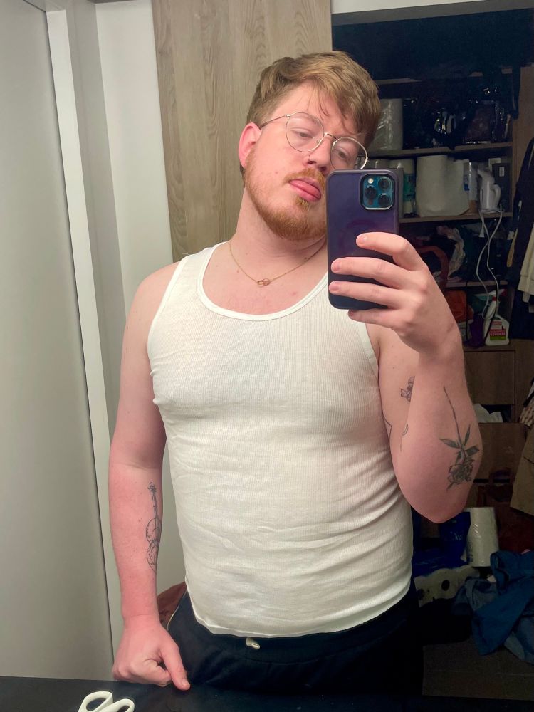 Standing in front of the bathroom mirror in a white form fitting tank top, relaxed pose and sticking tongue slightly out. You can see the indentation of my nipples through the shirt 