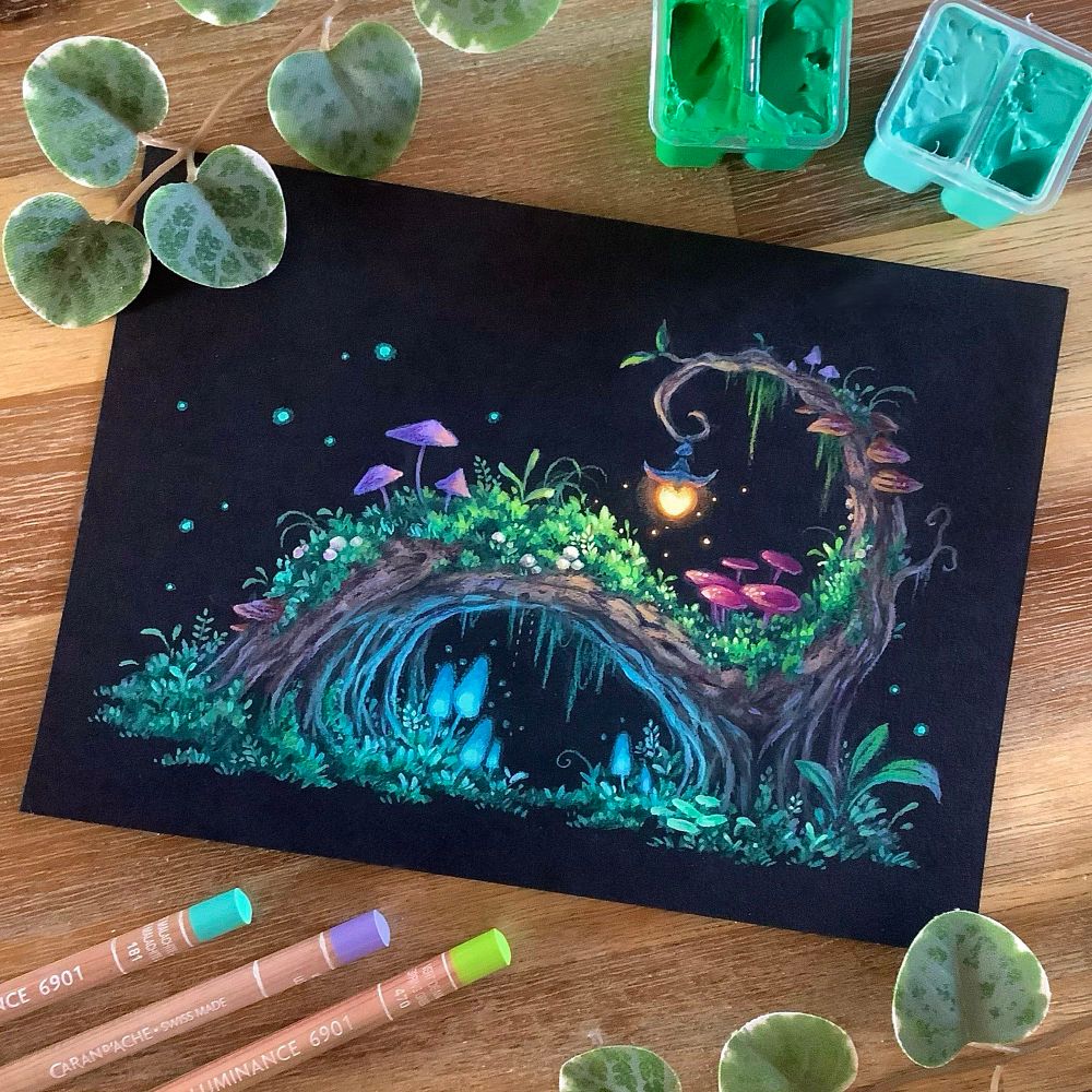 A photo of a landscape-format painting on black paper, placed on a wooden table and surrounded by jelly gouache tubs, coloured pencils, and leaves for decoration. The painting features a horizontally arching tree with a little spiral on top, to which a tiny lantern is attached, emitting a warm orange glow. The tree is overgrown with moss and different kinds of mushrooms, some of them bioluminescent, emitting a soft cold blue glow.