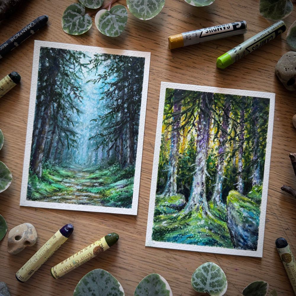 A photo of two portrait-format oil pastel paintings, placed in a scratched up wooden desk and surrounded by hag stones, branches, leaves, and oil pastels. The left painting features a dirt path bordered by moss and pine trees disappearing in thick fog; the right painting features warm yellow light filtering through conifers, moss growing at their base.