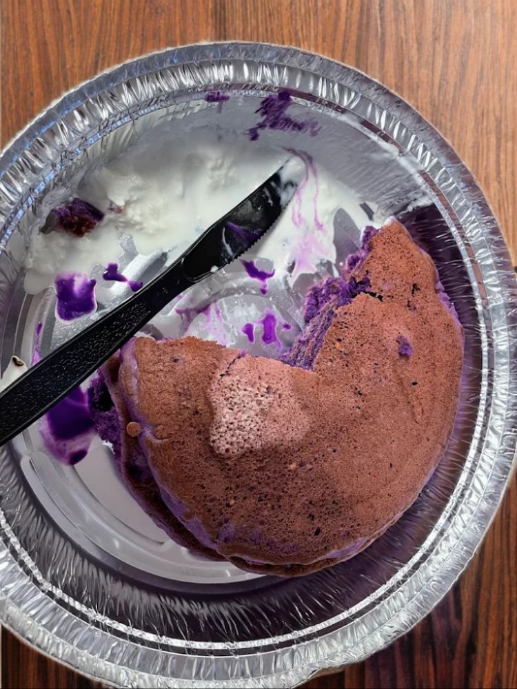 Ube pancakes w cream fillings quarterly eaten on a disposable plate kept on a wooden plate.