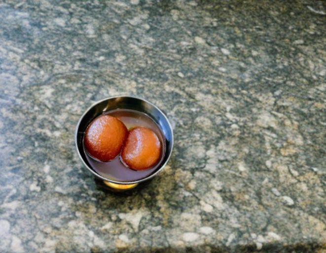 2 Gulabjamoon soaked a sugar syrup kept on a small bowl, placed on kitchen countertop.