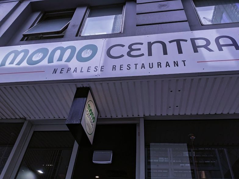 Sign for "Momo Central Nepalese Restaurant" displayed above the entrance of a building, with an additional small sign near the door.