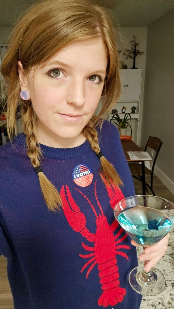 Wowzerz wearing a blue sweater with a lobster on it. She is holding a martini glass with a blue drink in it