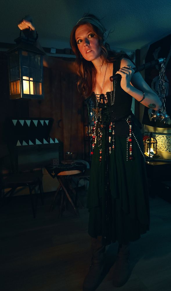 Wowzerz dressed like an elf and holding a lantern out with her right hand and a medieval triple mace over her left shoulder. There is a mimic chest lurking behind her