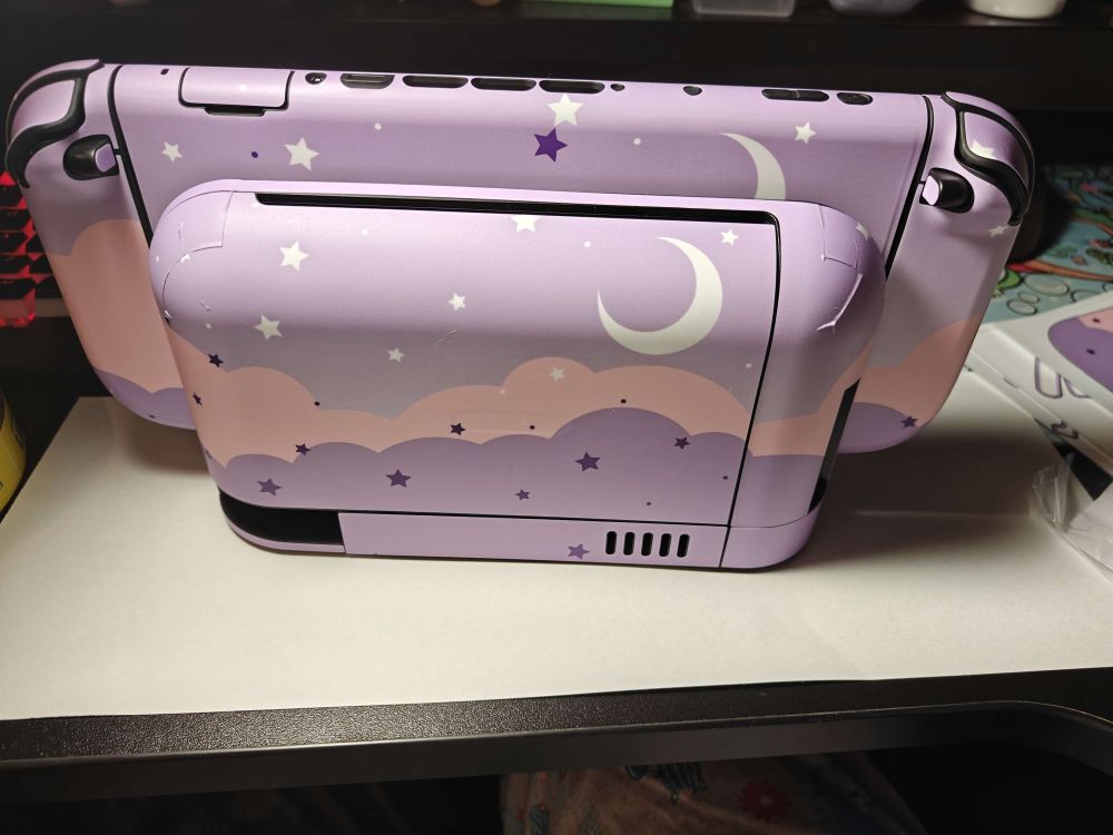 The back of a docked Switch 2 with a decal on it depicting a dreamy purple night sky with stars, crescent moon, and pink/purple clouds.