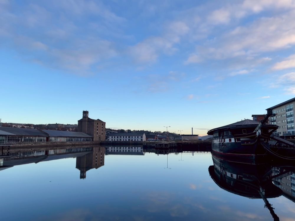 A view across still water at Dundee's City Quay, facing the Clocktower Building and Unicorn ship.