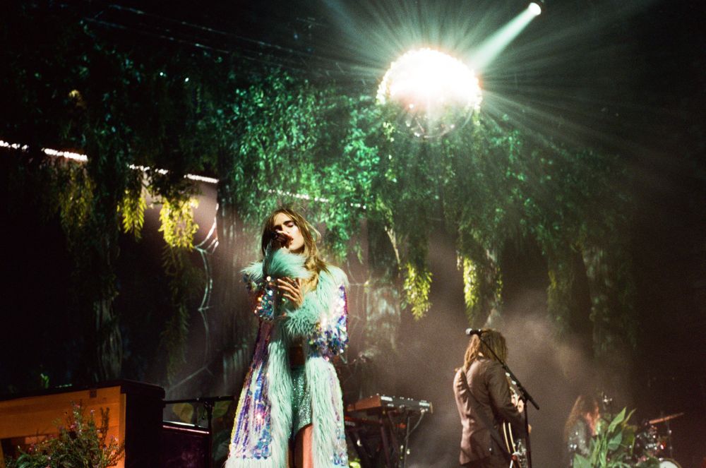 Suki Waterhouse singing with a disco ball lighting behind her.