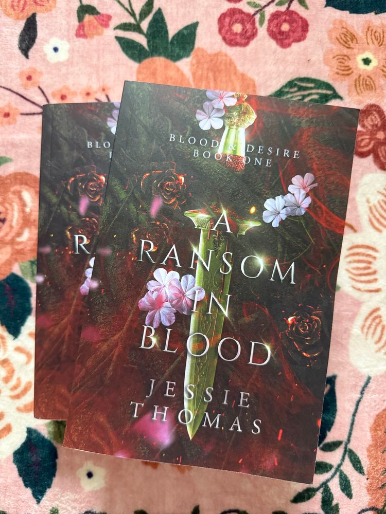 Paperback copies of the book stacked on top of each other against a pink floral rug.