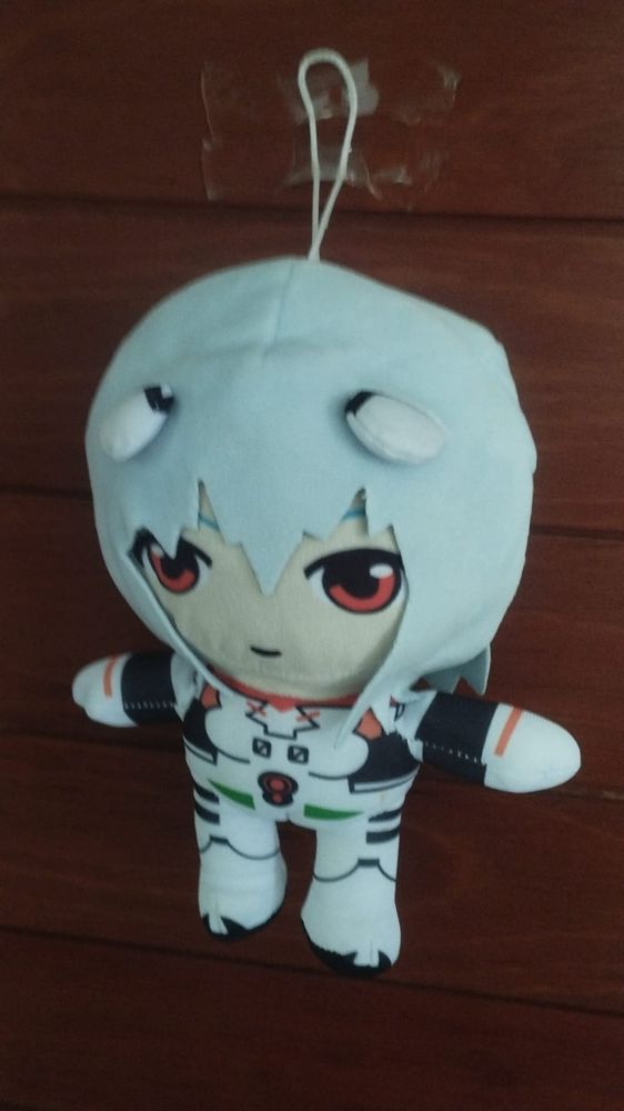 Imagem de uma pelúcia pequena e cabeçuda da personagem Rei Ayanami do Evangelion pregada com durex numa porta de madeira.