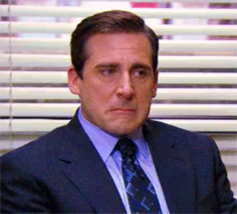 a man in a suit and tie is sitting in front of blinds