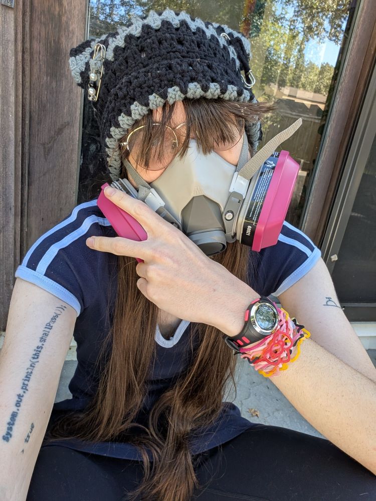 sitting in front of a glass door wearing the same dress, a black and gray striped cat-ear hat, a ventilator with pink cartridges, and a bunch of sillybands