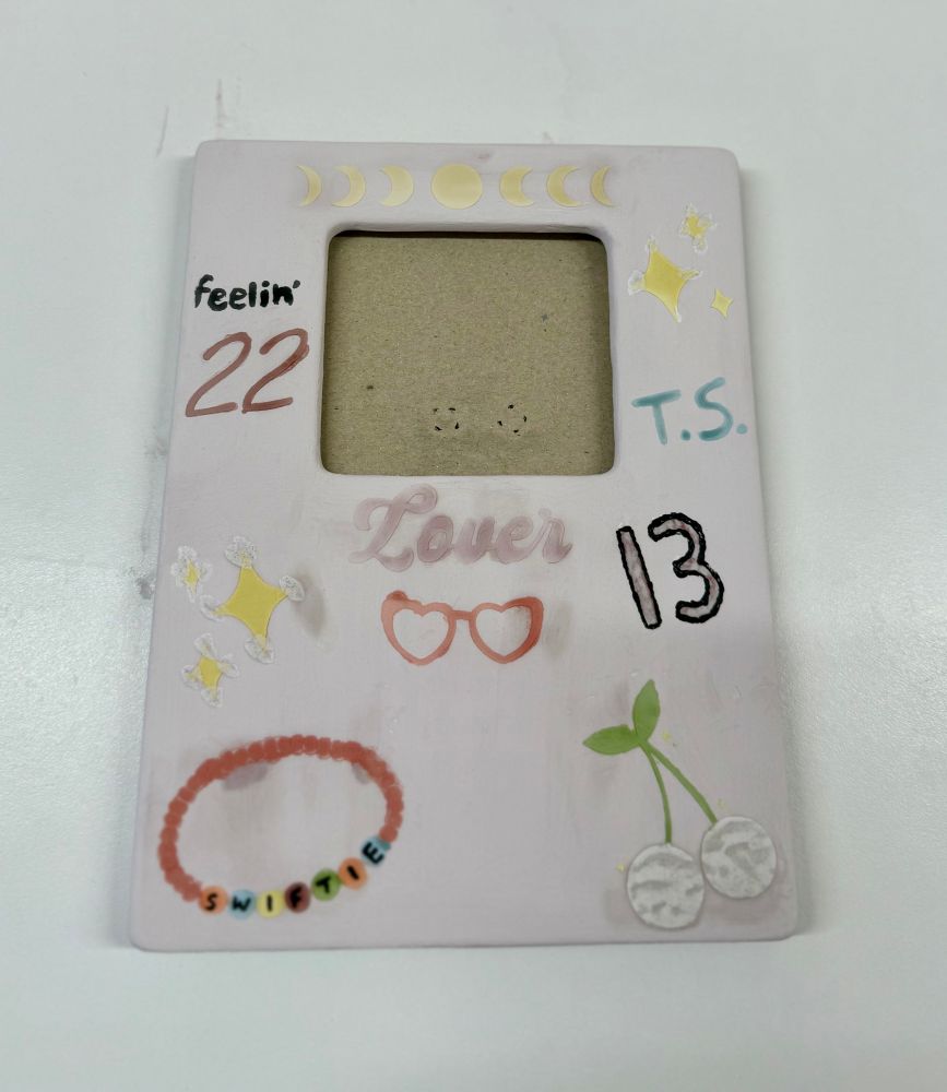 A photo frame painted with Taylor Swift themed symbols and objects before it’s been glazed in the kiln 