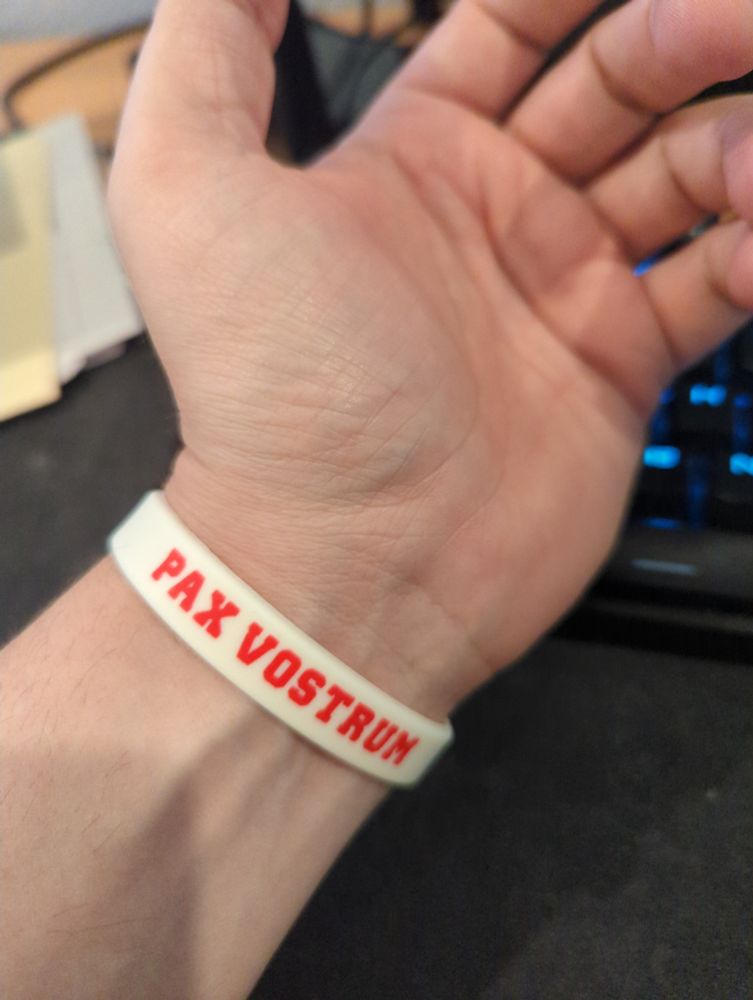 Hand with a wrist band that says "PAX VOSTRUM"