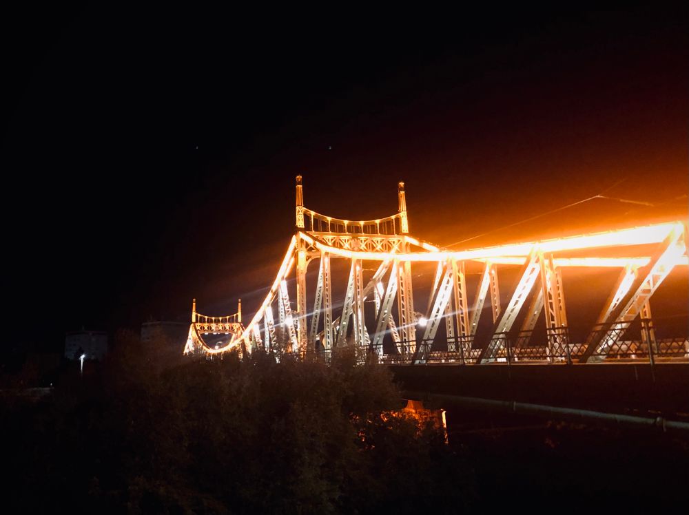 Blick bei Nacht auf eine Brücke mit von rötlichem Licht erleuchteten Stahlträgern.