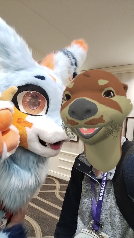Portrait selfie of a sky-blue and orange fursuiter with with someone wearing a digitally superimposed river otter head.