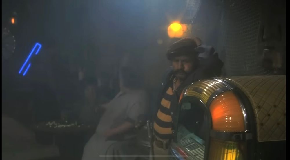 Mustachioed chap standing by a jukebox in the film Airplane!