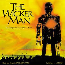 Wicker Man LP cover. Yellow background with giant straw man on it. People wearing deer antlers congregate at its feet. 