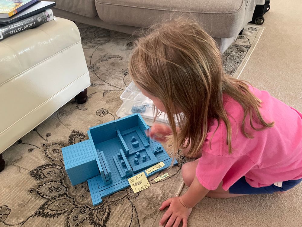 Girl pointing out parts of building she made with blue blocks usually used to represent place values in match education