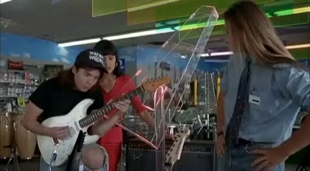 a man is playing a guitar in a store while a woman stands behind him .