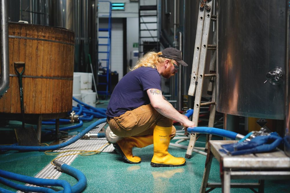 Christie from Abbeydale crouching down to connect a hose in the brewery