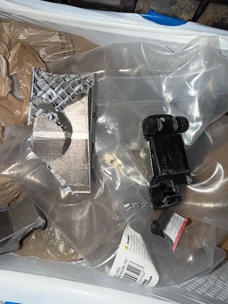 A 3-D printed model of a Nazi truck with the hot wheels version of the Nazi truck, crushed by a blacksmith hammer and put in the trash.