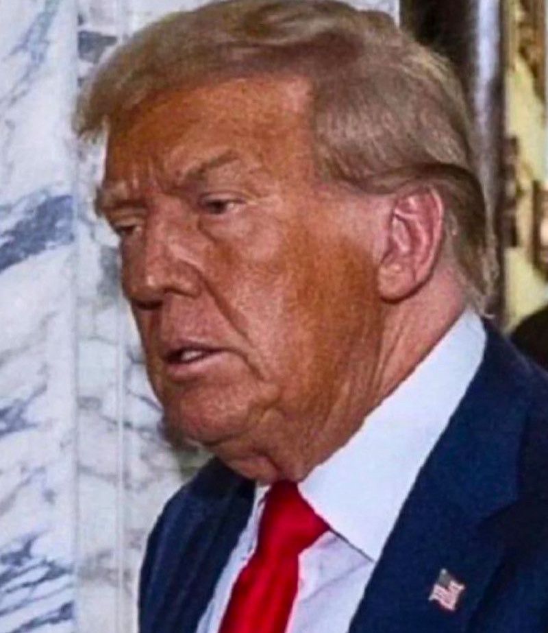 A head shot photo of the 47th President Of The USA. It shows his face covered with dark 'bronzer' hastily and sloppily applied. There are noticeable, farcical gaps in application and he really does not look well.