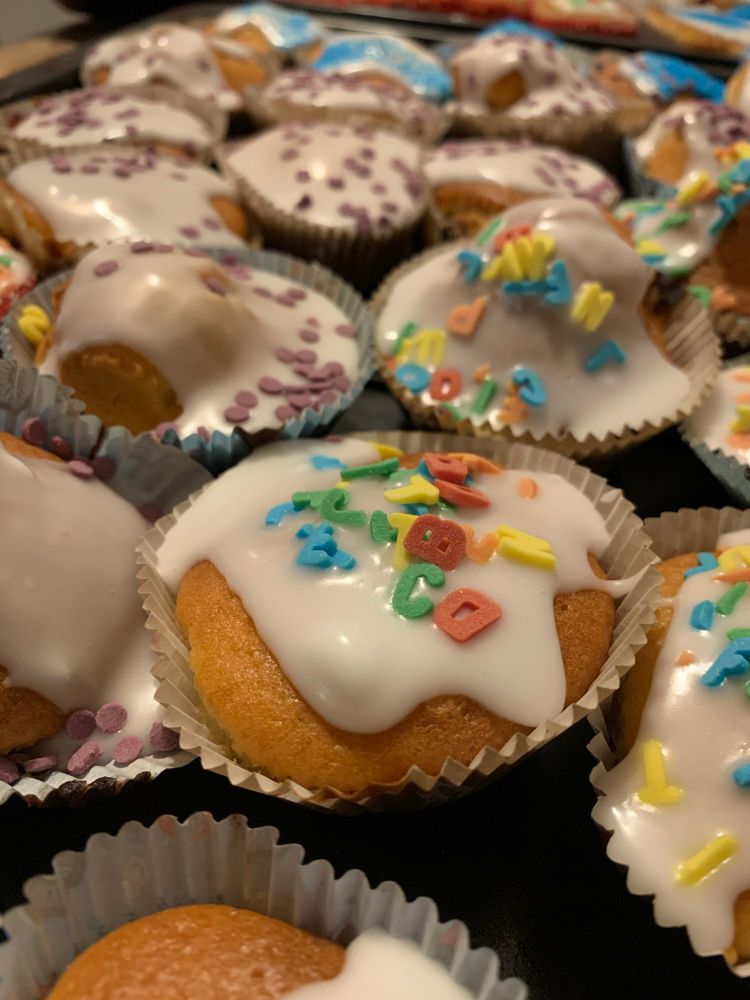 Ein grosses Blech mit hellen Muffins mit Zuckerguss und bunten Streuseln, z.B. Buchstaben. 