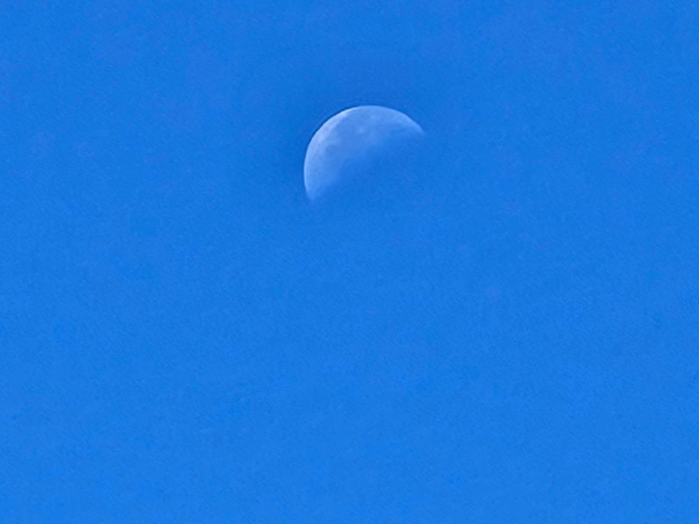 The 3/4 moon in daylight blue sky.