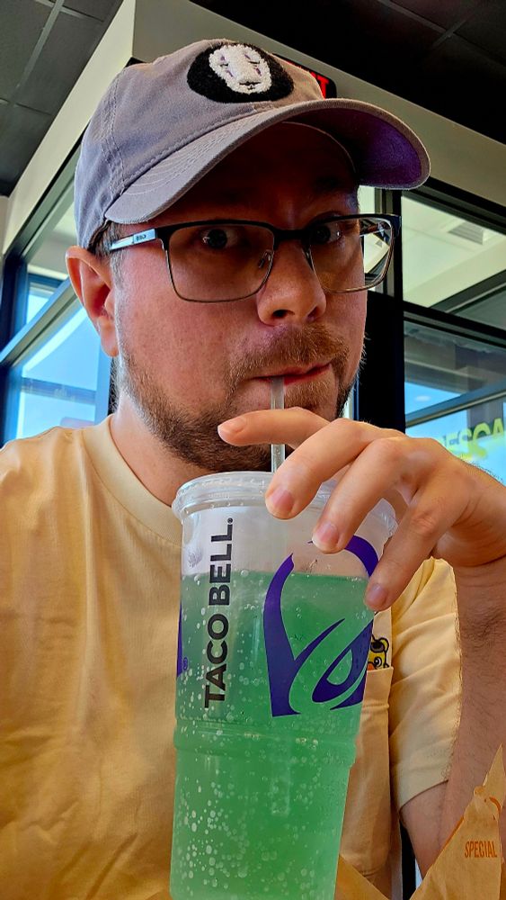 Person sipping Baja blast at taco bell in a ghibli hat and yellow shirt