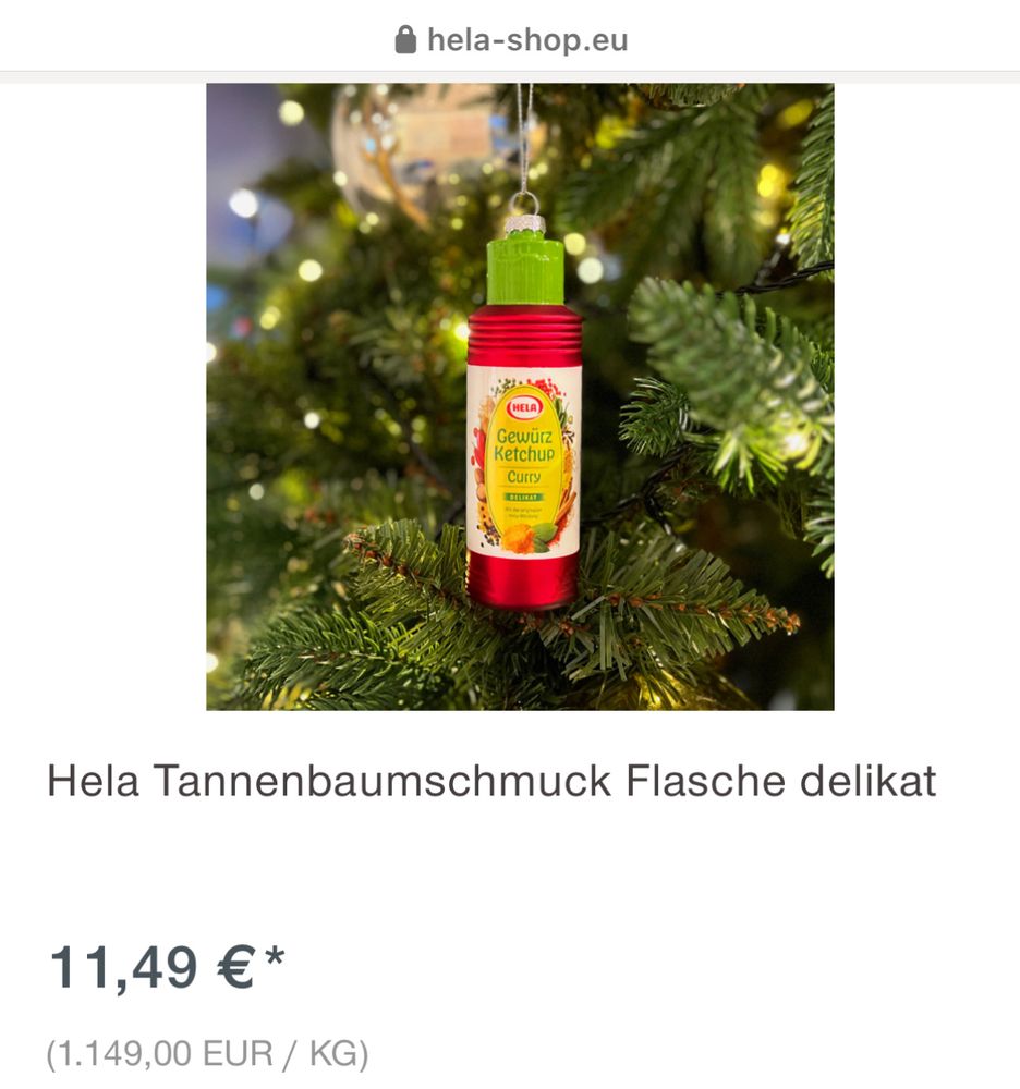 Screenshot aus dem Hela Shop: Eine Weihnachtsbaumkugel (auf Produktbild hängt sie festlich in einem Tannenbaum, verschwommene Lichter im Hintergrund) in Form einer Hela Gewürzketchup-Flasche. Produktbezeichnung: Hela Tannenbaumschmuck Flasche delikat Preis: 11,49 Euro