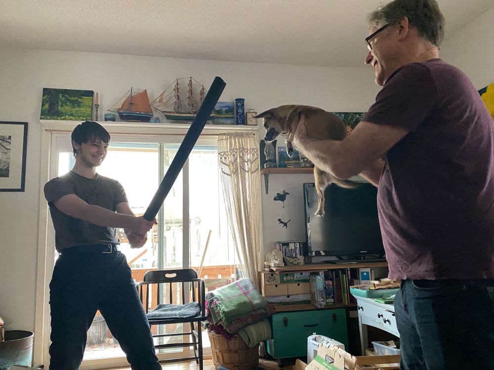 Tall teenager brandishes foam boffer sword at man holding confused-looking chihuahua in front of him defensively. 