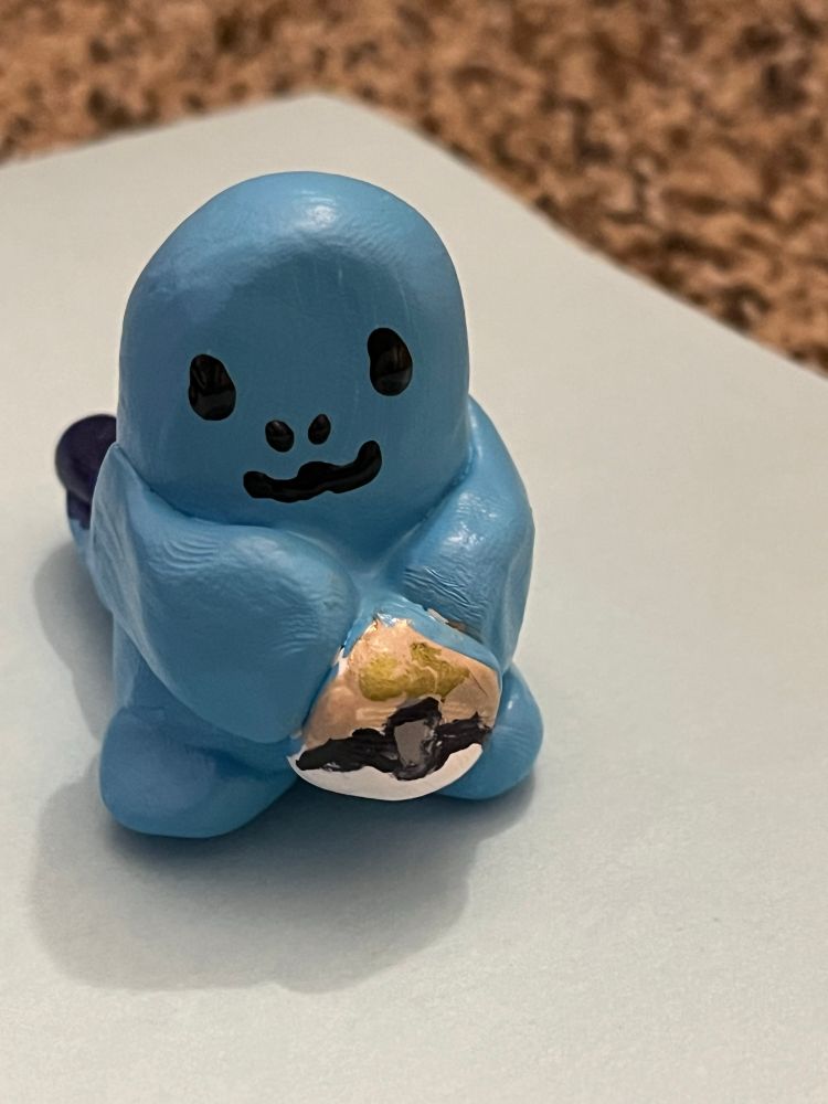 Clay figurine of the Pokemon Quagsire, a lil blue gremlin guy, holding a GS Ball