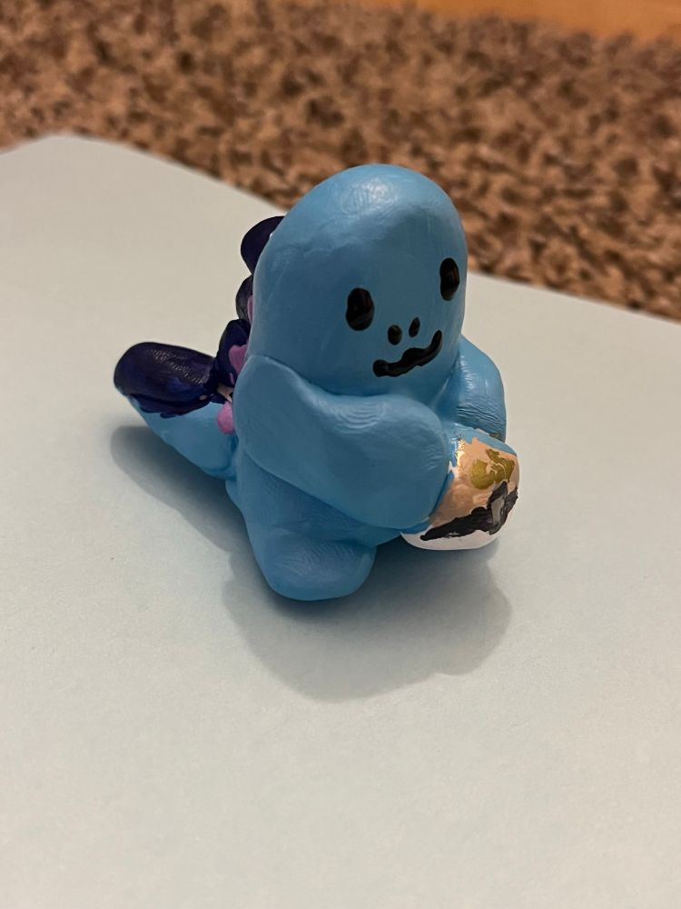 Clay figurine of the Pokemon Quagsire, a lil blue gremlin guy, holding a GS Ball