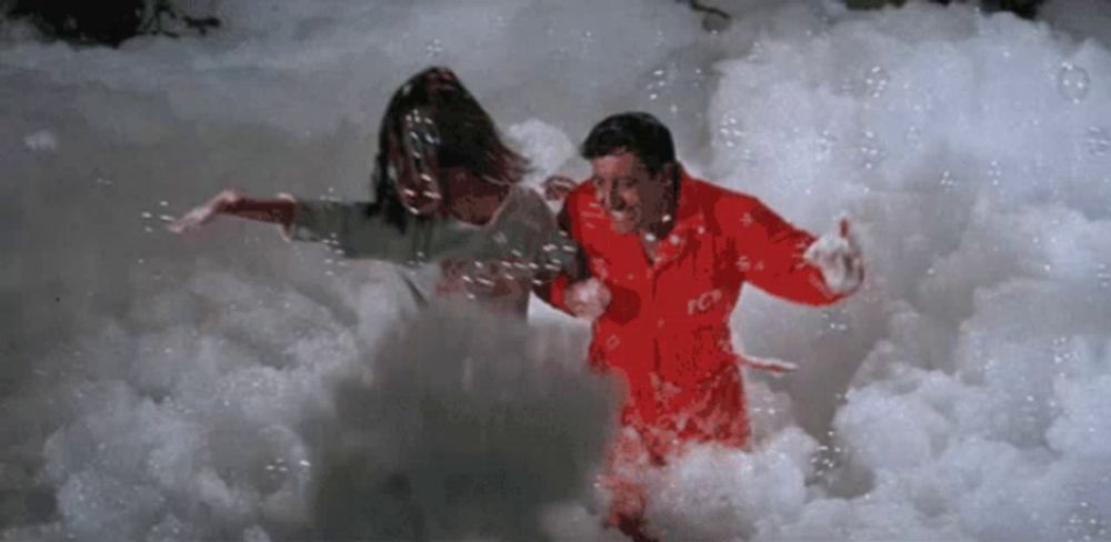 a man and a woman are in a pool of foam and the man is wearing a red jacket that says ice on it