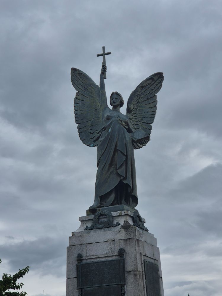 An angel, holding a cross high in one hand, her wings spread, a bible in her other hand, with her top pulled to her waist and her tits out