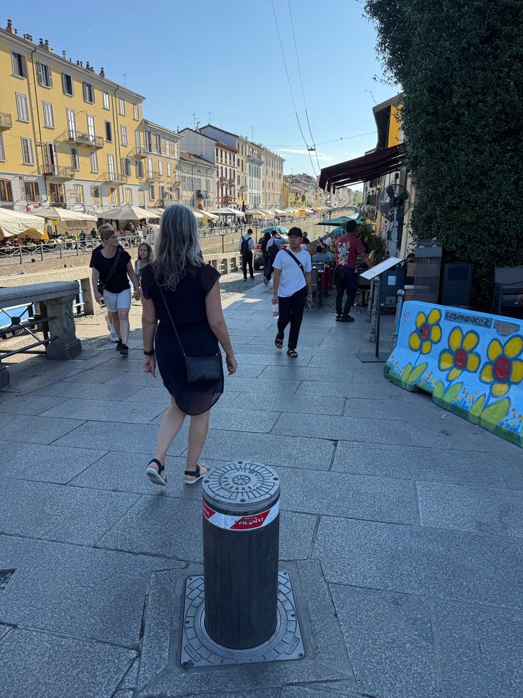 Photo of Navigli neighbourhood with retractable bollard in the foreground and a car’s taillights hidden behind a throng of pedestrians.