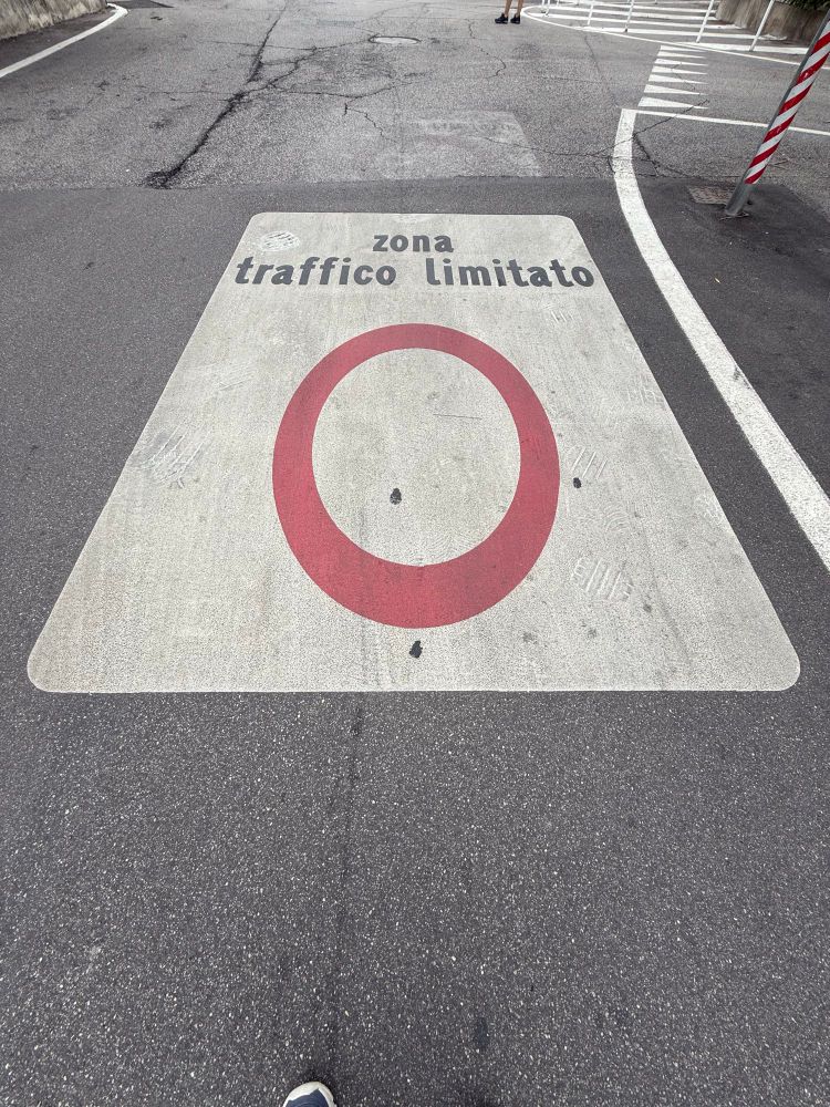 Sign on pavement in Italian town with red round circle symbol and writing that translates to ‘limited traffic zone’